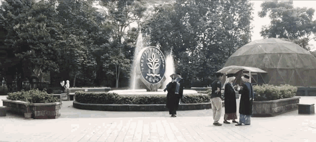 a group of people standing in front of a fountain with the university of indonesia logo