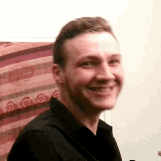 a man wearing a black shirt is smiling in front of a colorful striped curtain