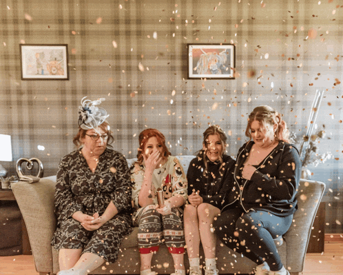 four women sitting on a couch with confetti falling on them