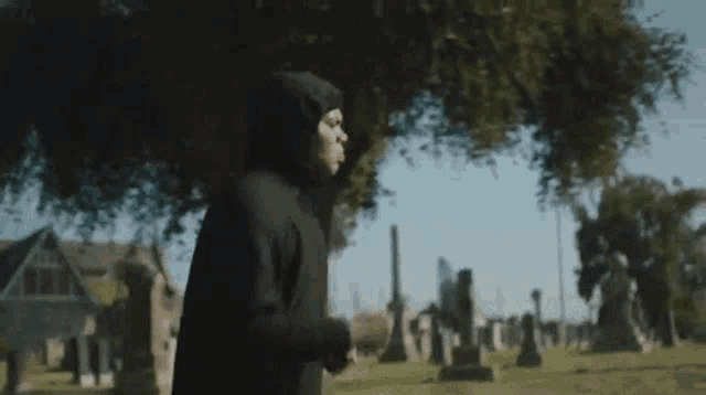 a man in a hooded sweatshirt is running through a cemetery .