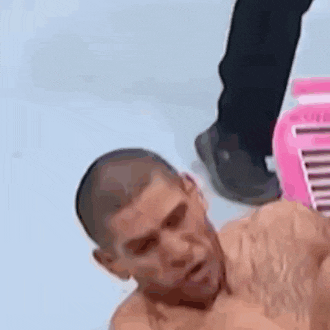 a man without a shirt is laying on the floor next to a pink box .