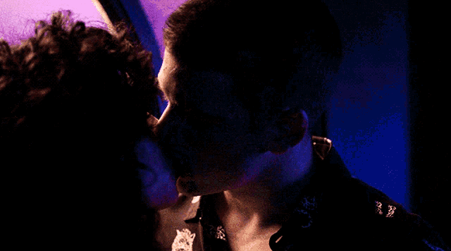 a man and woman are kissing in a dark room with a blue light behind them