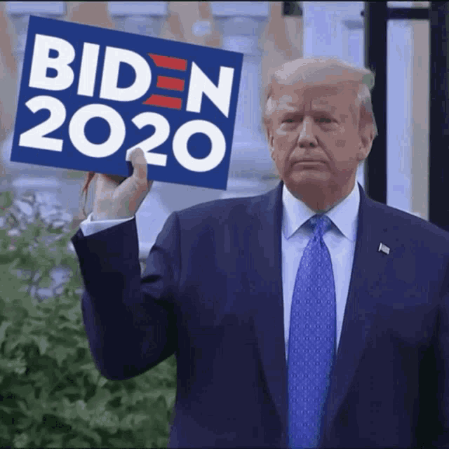 a man in a suit and tie holds up a sign that says biden 2020