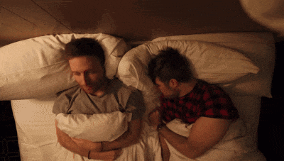 two men are laying in bed holding hands