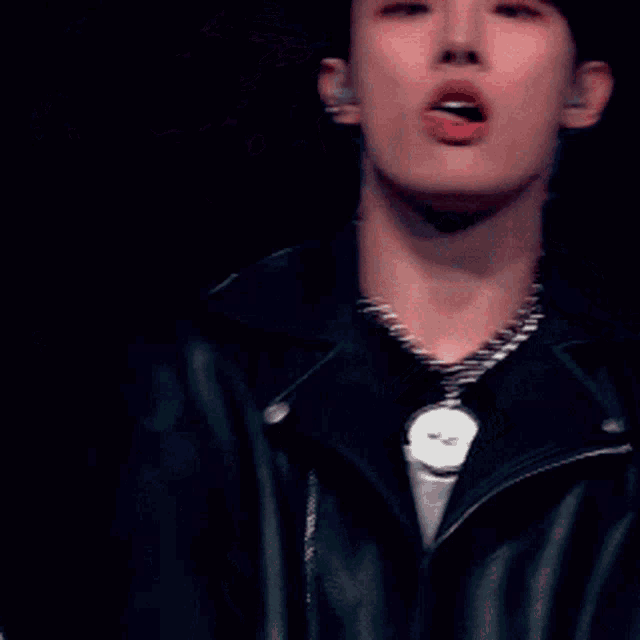 a man wearing a necklace and a leather jacket is making a peace sign with his hands