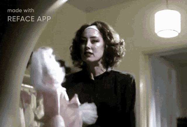 a woman in a black dress is holding a pink doll in a bedroom .