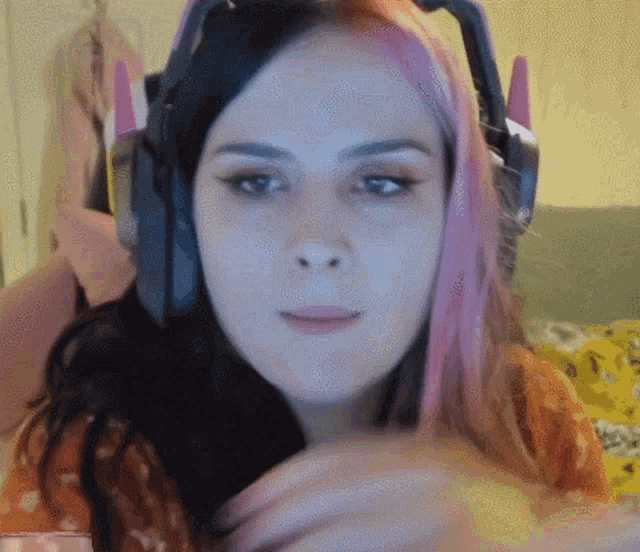 a woman with pink hair wearing headphones looks at the camera