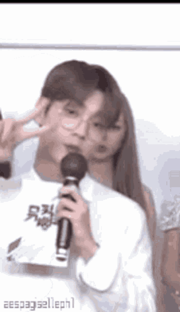 a man is holding a microphone and giving a peace sign while a woman looks on .