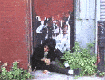 a man sits on the sidewalk in front of a red door with a sticker on it that says btl