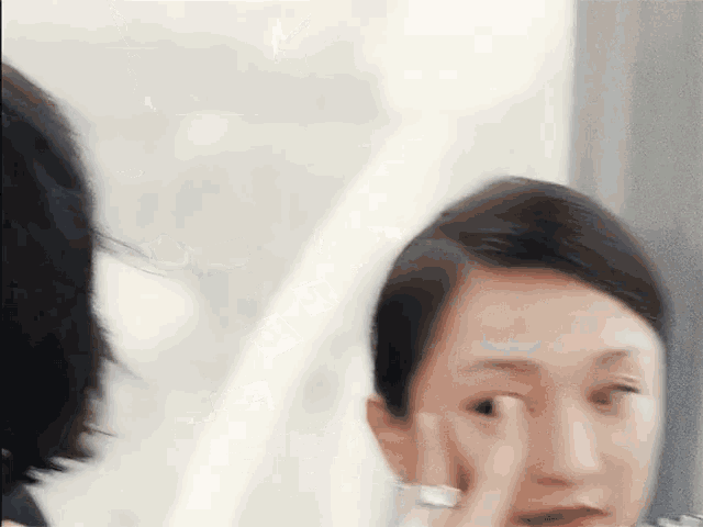 a woman is applying makeup to her face in front of a mirror while another woman looks on .
