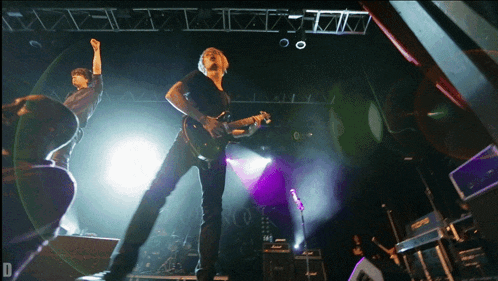 a man in a black shirt is playing a guitar on stage