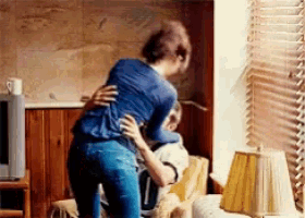 a woman is hugging a man who is sitting on a couch .