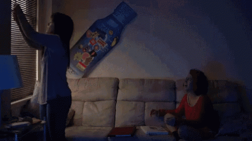 two women are sitting on a couch in a living room with a large poster on the wall that says ' sprite ' on it