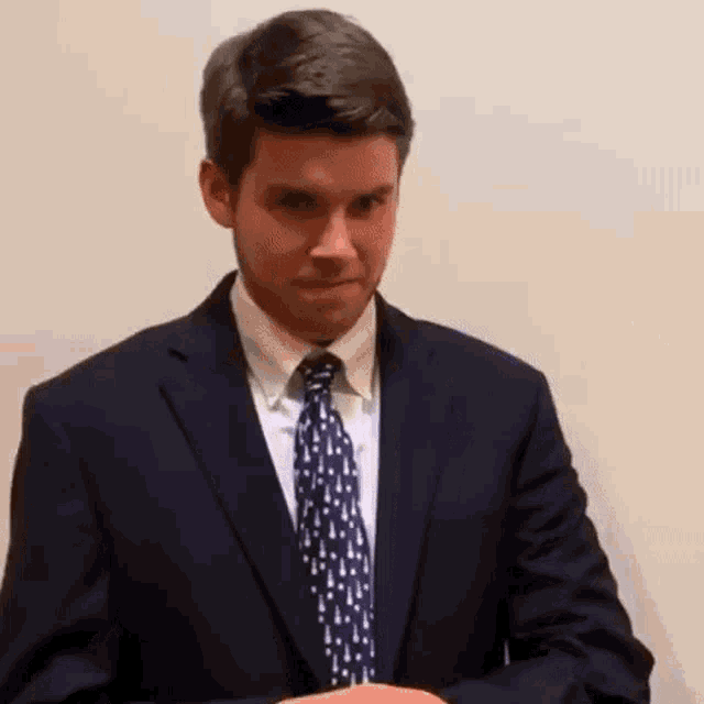 a man in a suit and tie is standing in front of a wall .