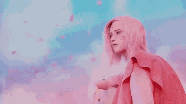 a woman with pink hair is standing in front of a pink background .