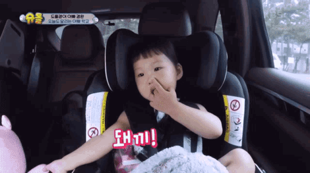 a little girl is sitting in a car seat with a sign that says warning