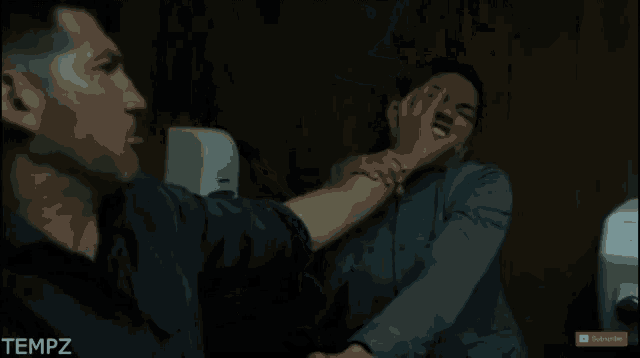 a man is holding another man 's arm in a bathroom with a subscribe button on the bottom
