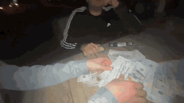 a man wearing a black adidas shirt is sitting at a table with a bunch of money on it