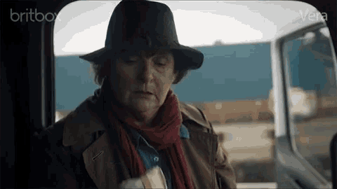 a woman wearing a hat and scarf is sitting in a car with britbox written on the bottom right