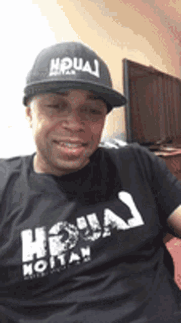 a man wearing a hat and a t-shirt with the word houai on it is smiling .