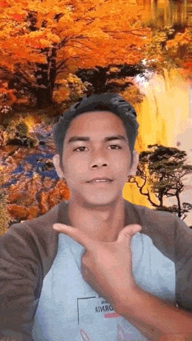 a man giving a peace sign in front of a waterfall with trees in the background