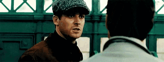 a man wearing a hat is talking to another man in a room .