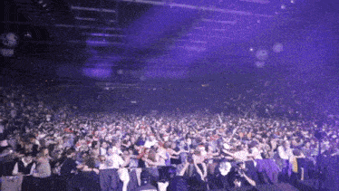 a crowd of people are gathered in a dark room with purple lights