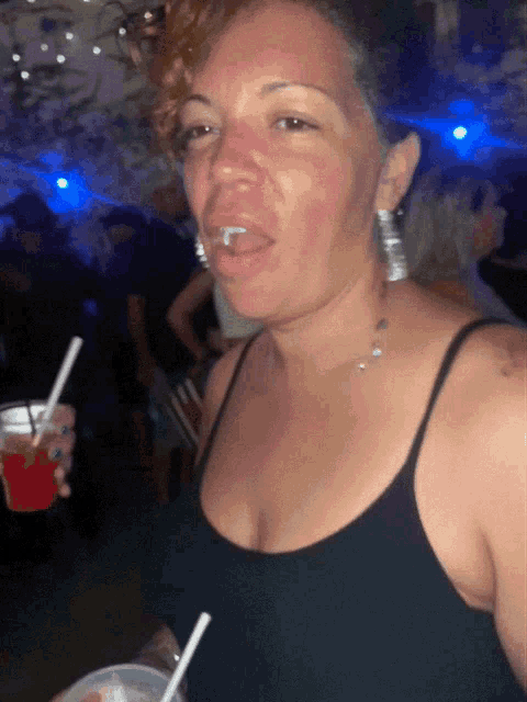 a woman in a black tank top is holding a plastic cup with a straw in her hand