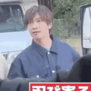 a man in a blue jacket is standing in front of a truck and looking at the camera .