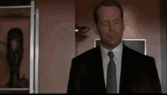 a man in a suit and tie is standing in front of a shelf with a mask on it .