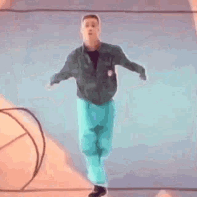 a man in a green jacket and blue pants is dancing in front of a drawing of a hand .