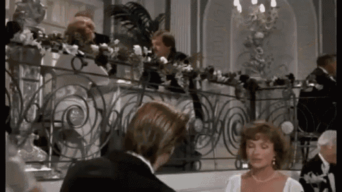 a man in a tuxedo and a woman in a white dress are standing next to each other on a balcony .