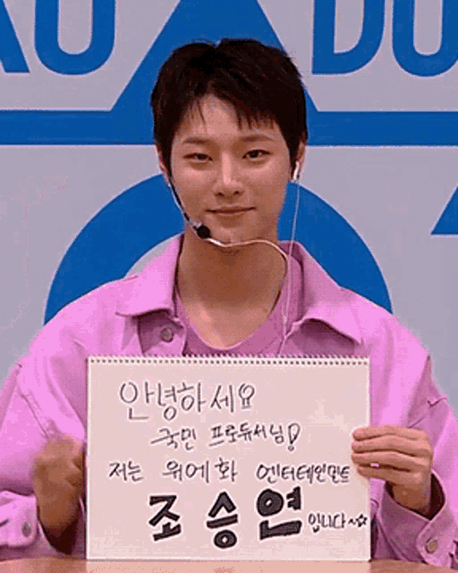 a young man in a pink jacket is holding a sign with korean writing