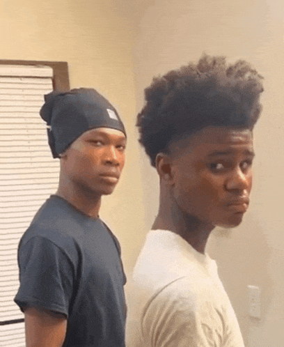 two young men are standing back to back and one has a beanie on his head