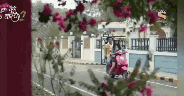 a woman is riding a scooter down a street with flowers in the foreground and a sony channel logo in the background