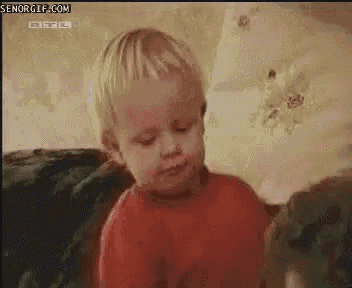a baby in a red shirt is sitting on a couch looking at something .