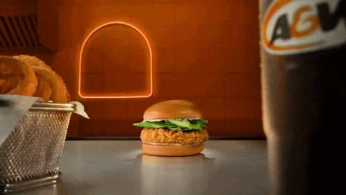 a chicken sandwich sits on a table next to a bottle of agw
