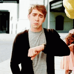 a man wearing a black cardigan and a grey shirt is looking at his watch