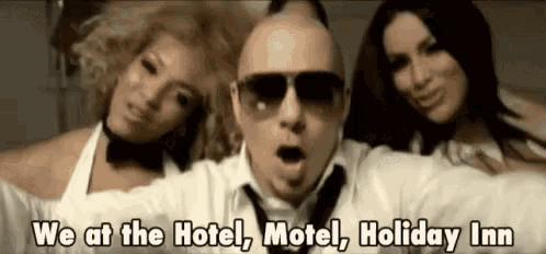 a man wearing sunglasses is standing next to two women and says `` we at the hotel motel holiday inn '' .