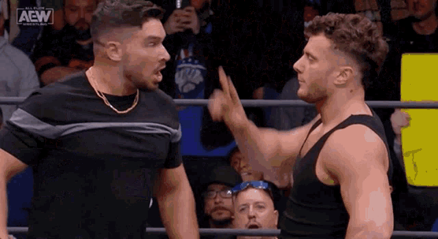 two men are fighting in a wrestling ring while a crowd watches .