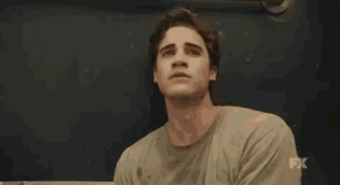 a man in a dirty shirt is sitting in front of a blackboard and looking at the camera .