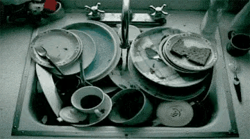 a kitchen sink filled with dirty dishes , cups , and spoons .