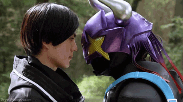 a man wearing a purple helmet is looking at another man wearing a black jacket