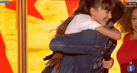 a girl is hugging a man on a stage with the number 1 on the screen behind them