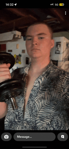 a man in a shirt is holding a dumbbell in front of a phone that says 14:32