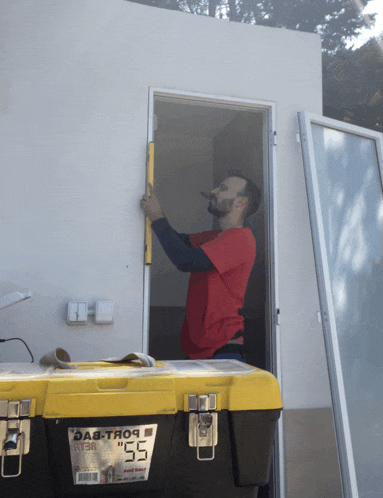a man in a red shirt is working on a door next to a toolbox that says ' das-trop ' on it