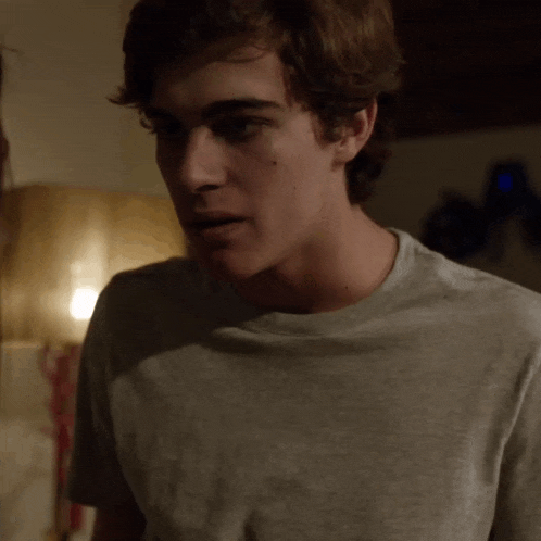 a young man wearing a grey t-shirt is standing in a dark room
