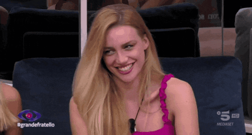 a woman in a pink top is smiling in front of a screen that says grandefratello