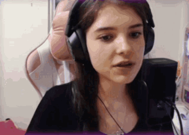 a girl wearing headphones looks at the camera with a pink chair in the background
