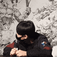 a man wearing a mask is sitting at a table in front of a wall .